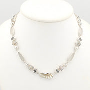 A silver-toned mixed-media necklace displayed on a white mannequin bust. The necklace features a variety of shells, small white pearls, and faceted white topaz.