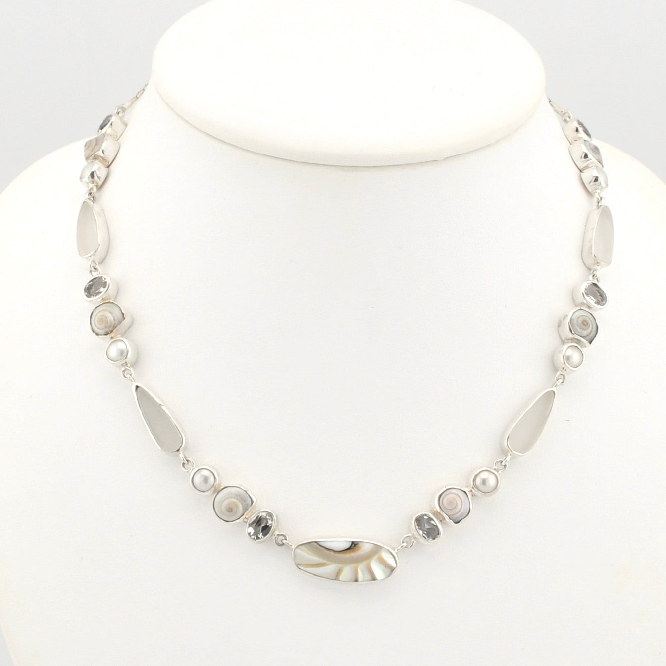 A silver-toned mixed-media necklace displayed on a white mannequin bust. The necklace features a variety of shells, small white pearls, and faceted white topaz.