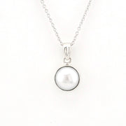 A silver necklace featuring a round, lustrous white pearl pendant set in a polished silver bezel, suspended from a delicate silver chain against a plain white background.