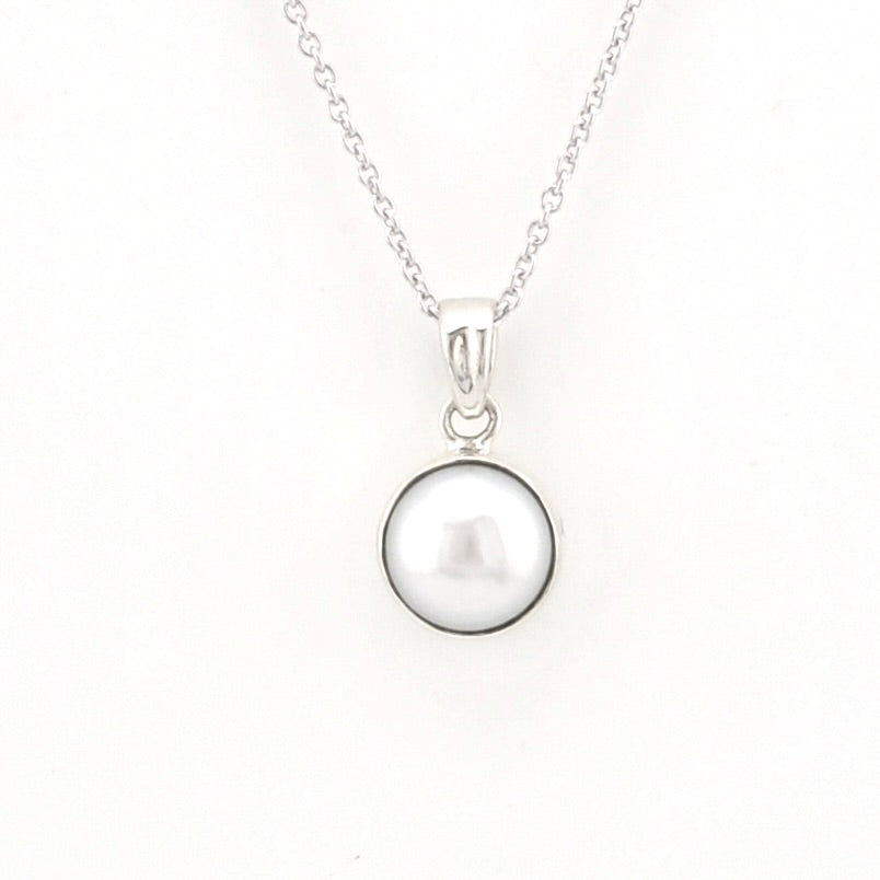 A silver necklace featuring a round, lustrous white pearl pendant set in a polished silver bezel, suspended from a delicate silver chain against a plain white background.