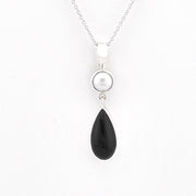 A silver pendant necklace featuring a round white pearl and a teardrop-shaped black stone, suspended from a delicate silver chain against a plain white background.