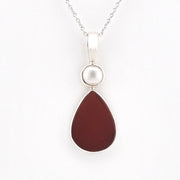 A silver pendant necklace featuring a teardrop-shaped dark reddish-brown stone and a small round white pearl-like bead, shown on a plain white background.