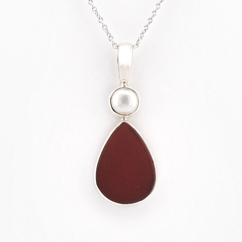 A silver pendant necklace featuring a teardrop-shaped dark reddish-brown stone and a small round white pearl-like bead, shown on a plain white background.