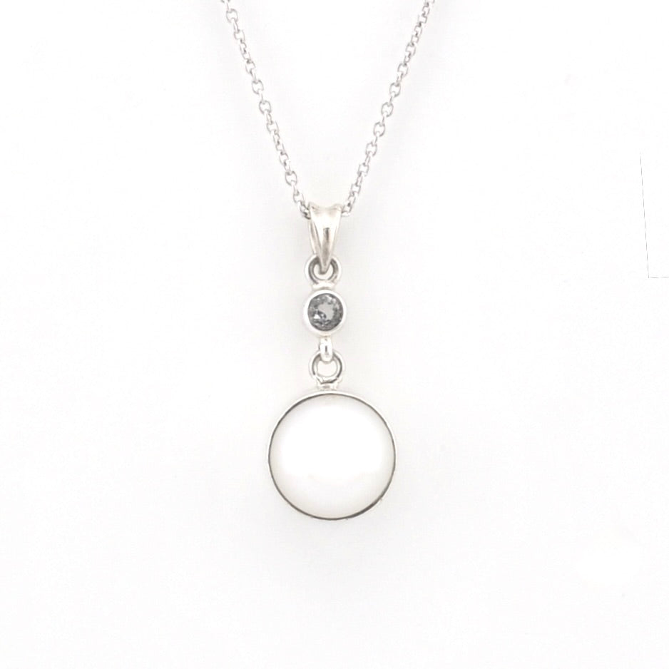 A silver pendant necklace featuring a large, smooth circular disc and a small round bezel-set dark stone, suspended from a delicate silver chain against a plain white background.