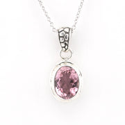 A silver pendant necklace featuring an oval-cut pink gemstone in a bezel setting, suspended from a delicate silver chain against a plain white background.