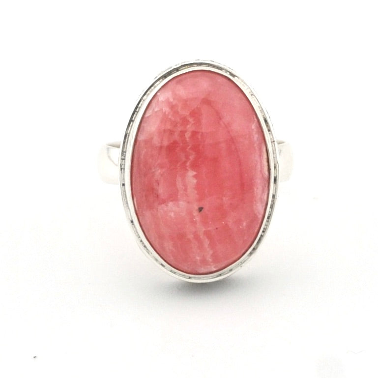 An oval ring featuring a pinkish-red cabochon gemstone in a silver bezel setting, shown against a plain white background.