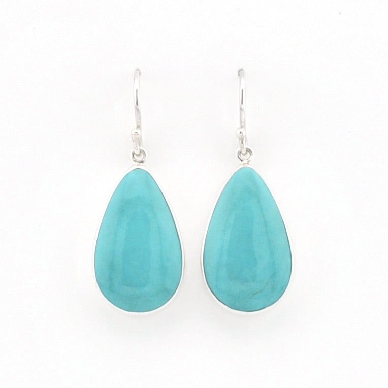 A pair of silver drop earrings featuring teardrop-shaped turquoise gemstones, displayed against a clean white background.