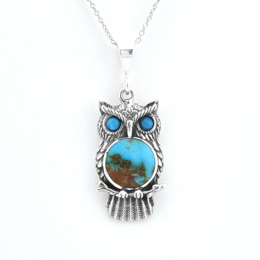 A sterling silver owl pendant necklace featuring a round turquoise stone with brown matrix inlay and two smaller blue turquoise stones for eyes, suspended from a silver chain on a white background.