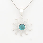 A sterling silver sunburst pendant necklace featuring a round turquoise stone in the center, suspended from a delicate silver chain against a plain white background.