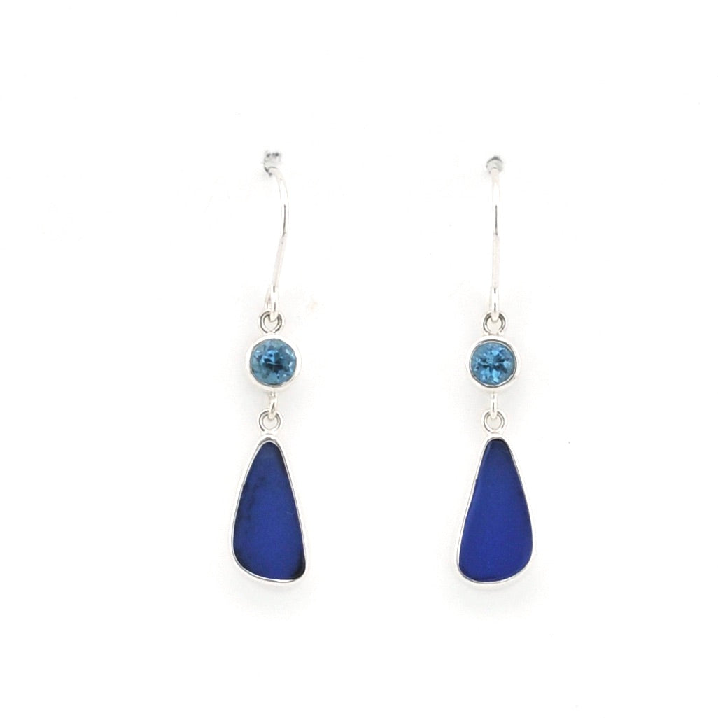 A pair of silver dangle earrings featuring a small round light blue gemstone and a larger teardrop-shaped dark blue sea glass below, set against a plain white background.