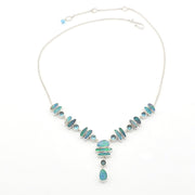 A silver necklace featuring a series of light blue and green opal set in silver, with a teardrop-shaped blue opal hanging at the center, displayed on a clean white background.