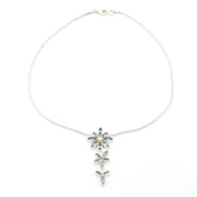 A delicate silver chain necklace featuring a vertical dangle pendant composed of three small flower motifs set with light blue marquise and round gemstones, shown on a plain white background.