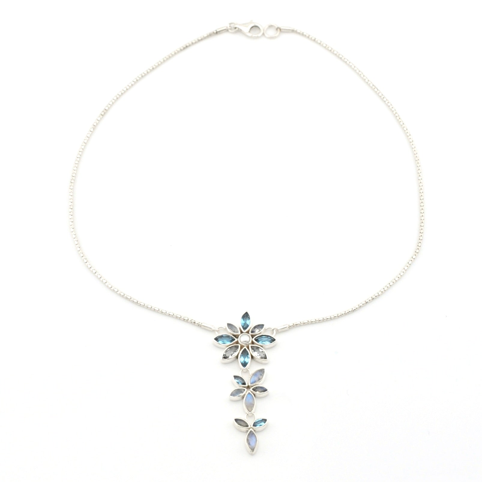A delicate silver chain necklace featuring a vertical dangle pendant composed of three small flower motifs set with light blue marquise and round gemstones, shown on a plain white background.