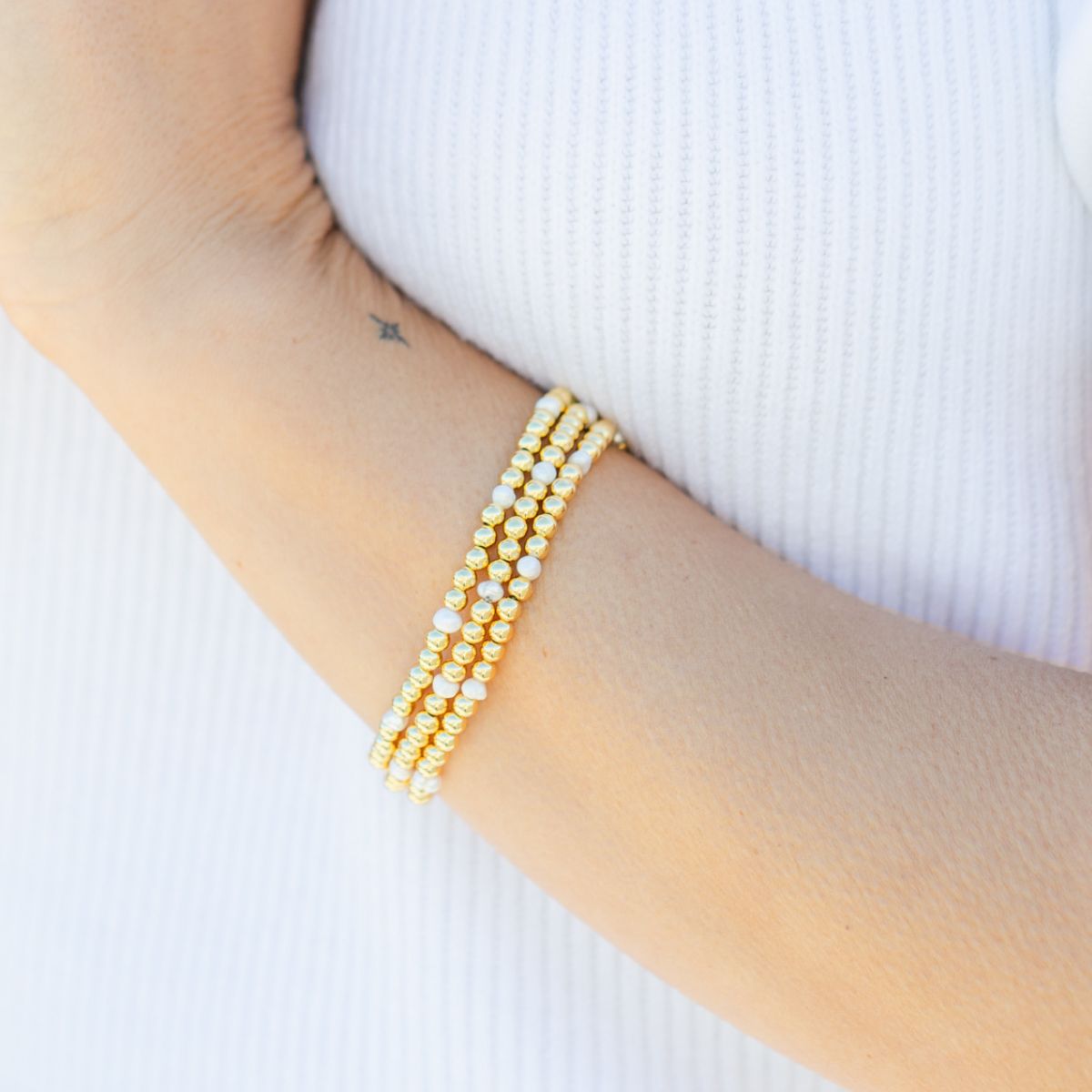 Gold bead bracelet with pearls staked on arm.