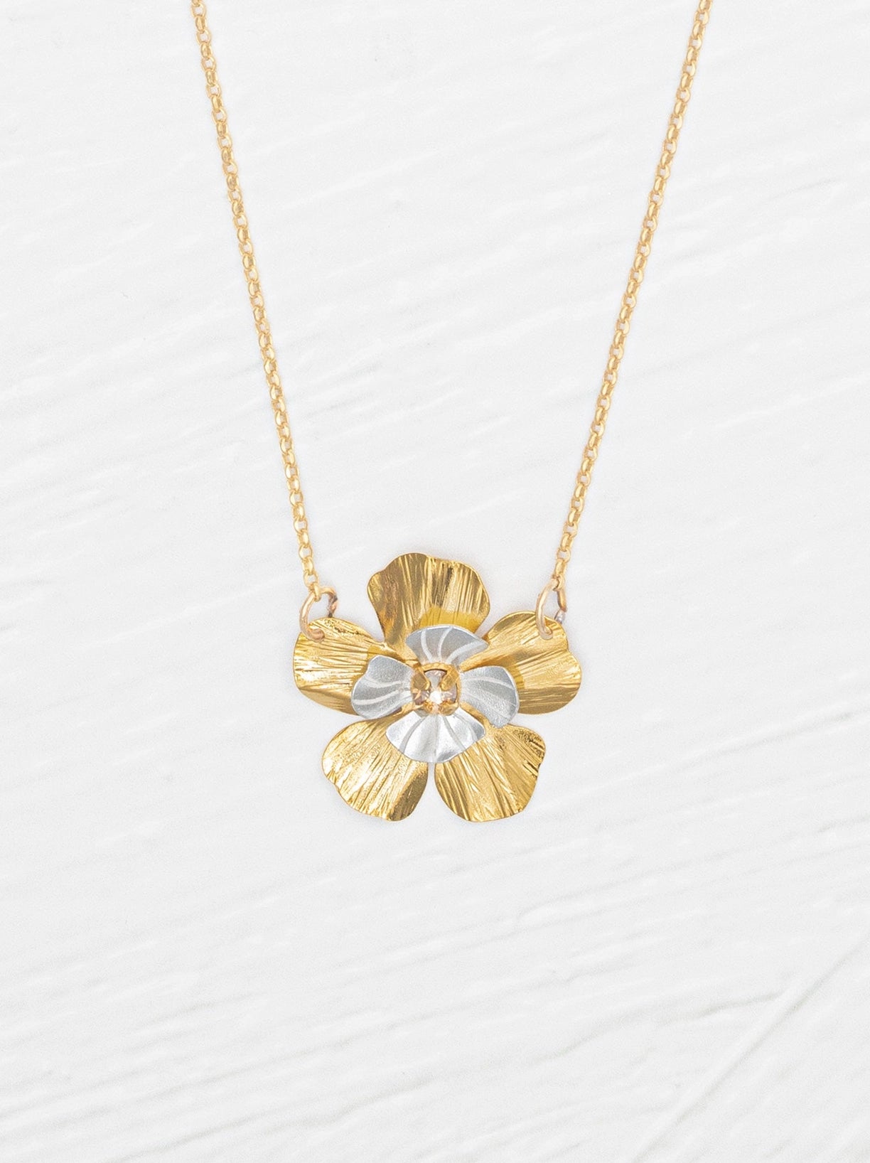 Gold and silver flower-shaped pendant on a chain against a white background