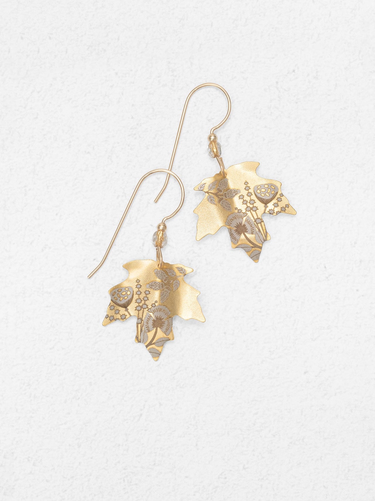 Gold leaf-shaped earrings on a light gray background