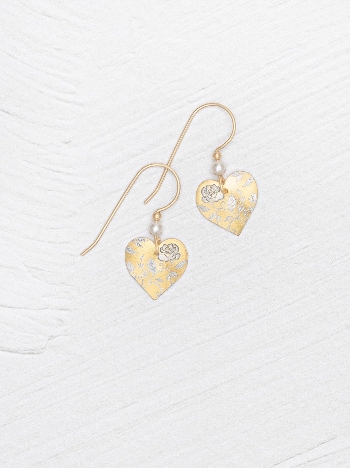 Heart-shaped gold earrings with floral details on a white background