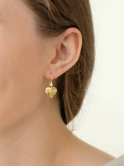 Close-up of a person wearing gold heart-shaped earrings on a plain background