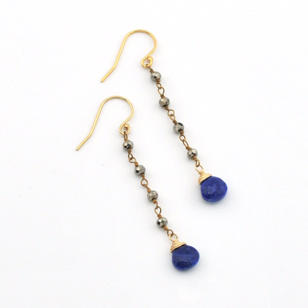 A pair of gold drop earrings with small metallic beads and deep blue oval gemstone pendants, shown on a plain white background.