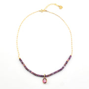 Necklace with purple beads and a pink gemstone pendant on a white background