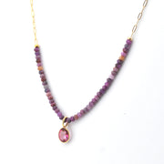 Necklace with purple beads and a pink teardrop pendant on a white background