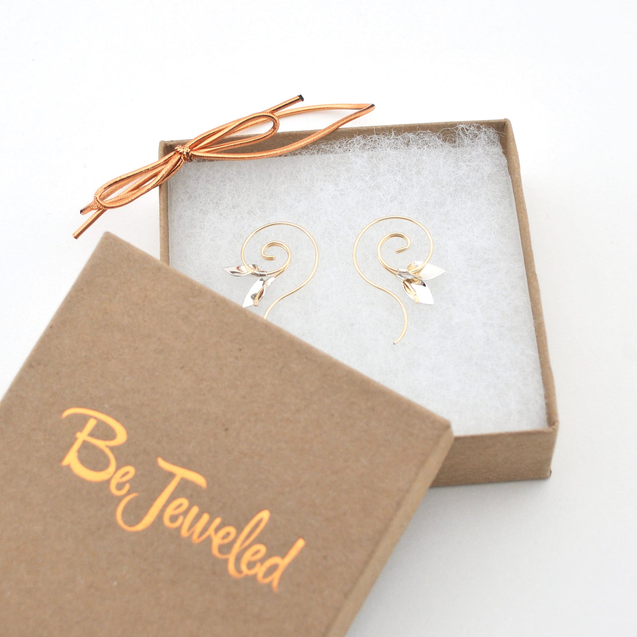 Gold earrings in a 'Be jeweled' box on a white background