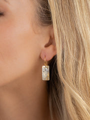 Close-up of a woman wearing gold earrings with a clear stone.