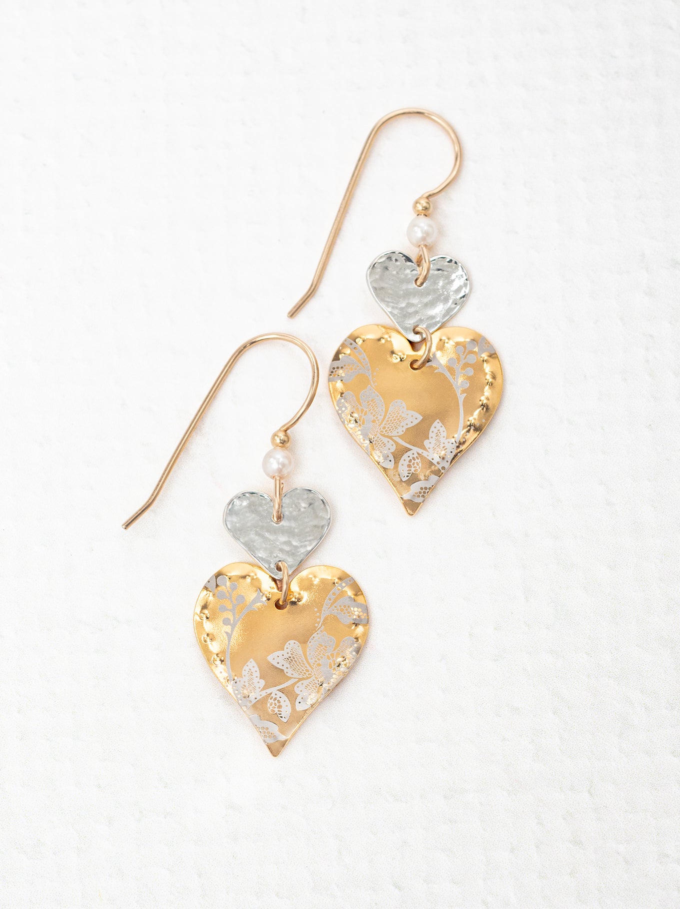 Heart-shaped earrings with gold, silver, and white floral patterns on a white background