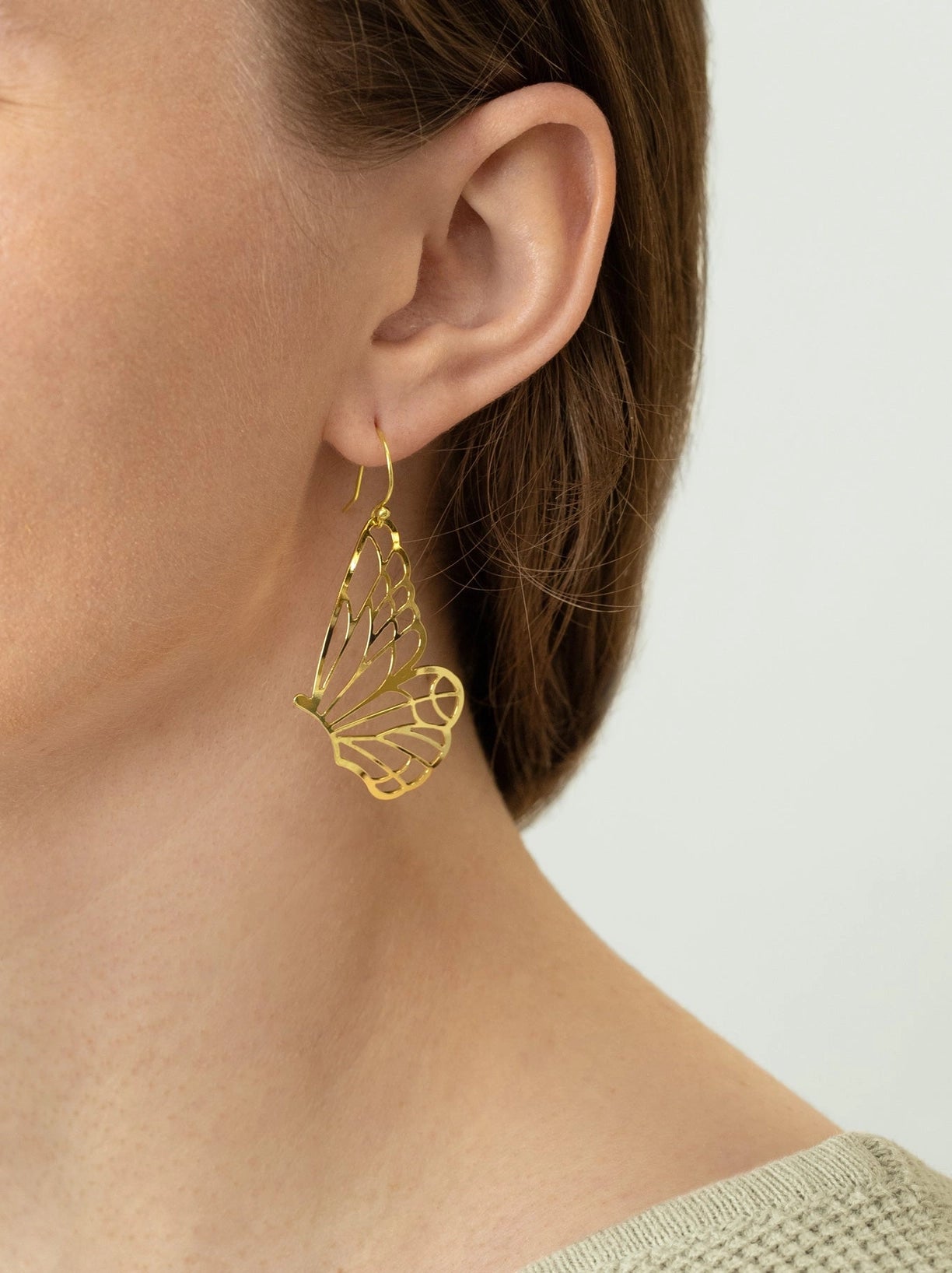 Gold butterfly earring worn by a person on a white background