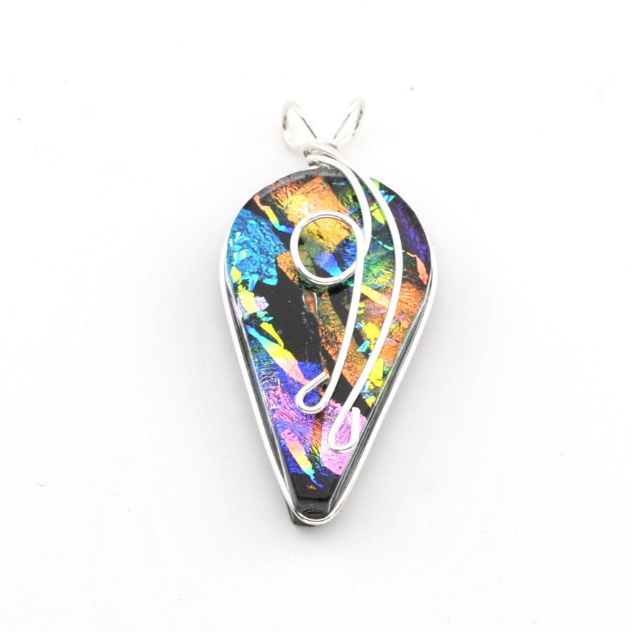 A teardrop-shaped pendant featuring a vibrant, iridescent dichroic glass with rainbow colors on a black base, wrapped with silver-colored wire and a small silver bail at the top, shown on a plain white background.