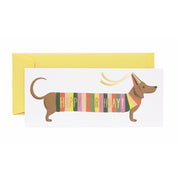 Birthday card with a dachshund wearing a colorful sweater and party hat, with a yellow envelope.