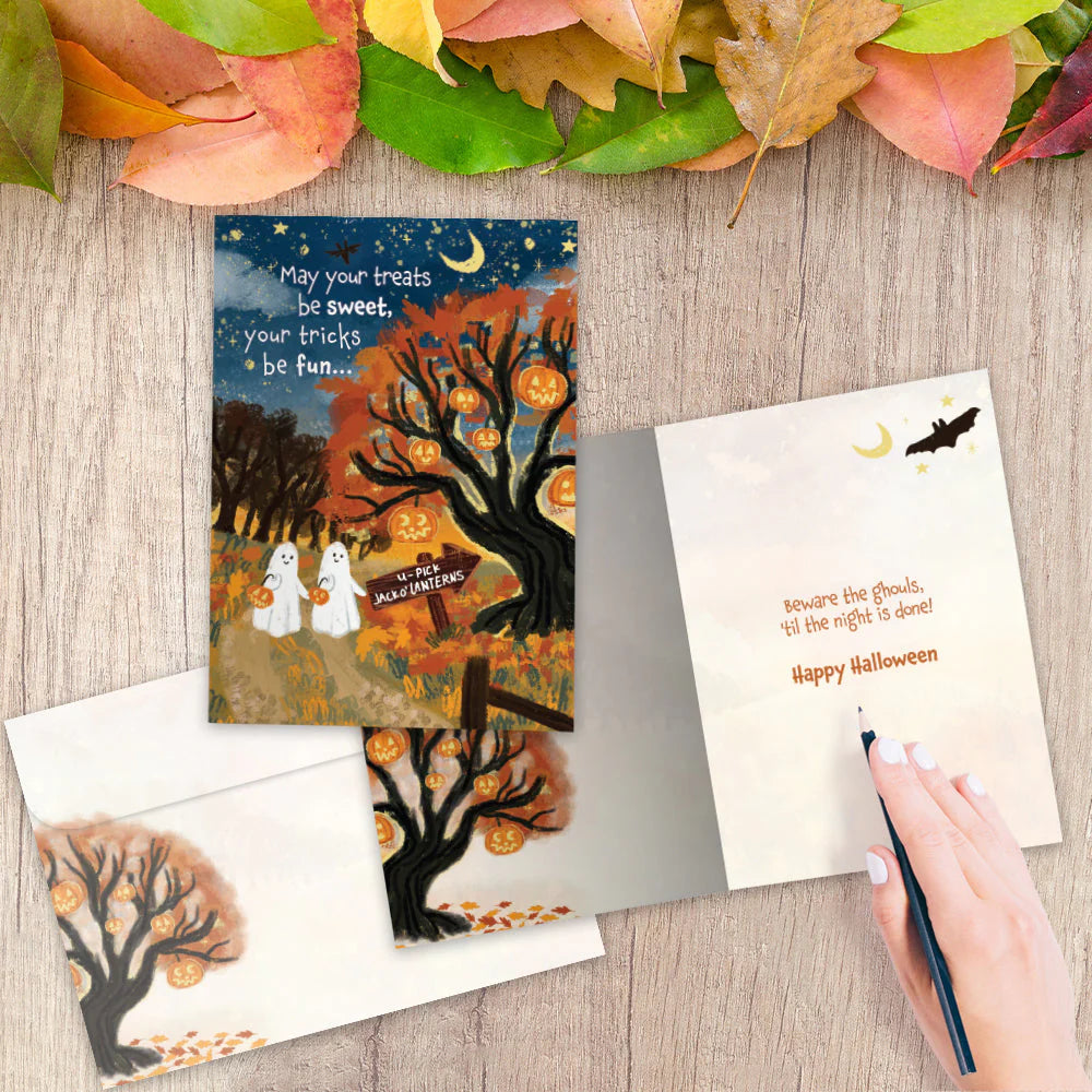 Halloween-themed greeting cards on a wooden surface with autumn leaves.