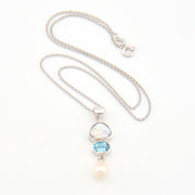Silver necklace with a pendant featuring a blue gemstone and pearl on a white background