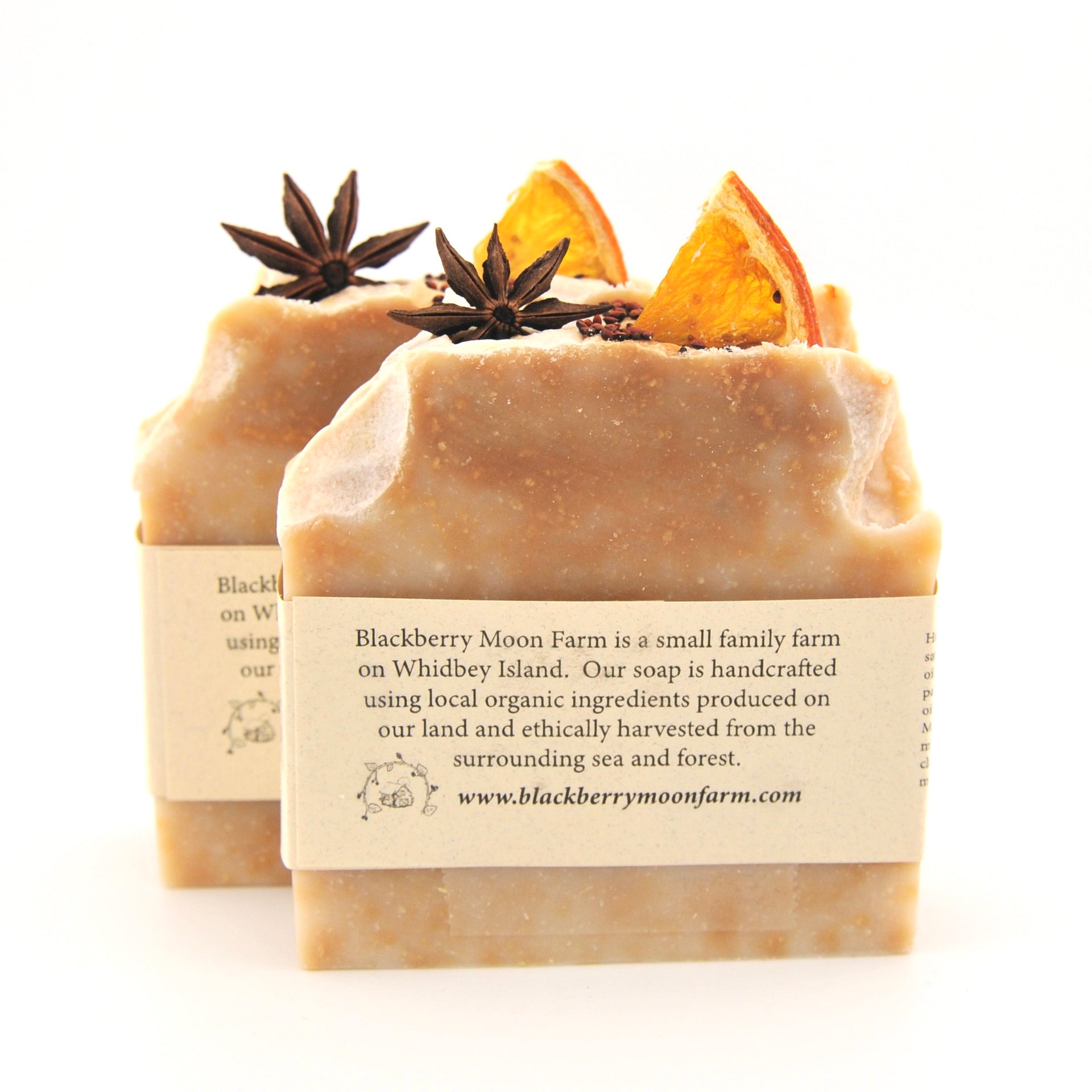 Two bars of soap with star anise and orange peel on top, featuring a label from Blackberry Moon Farm.