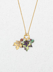 A gold chain necklace with three hanging niobium leaf charms in gold, green, and purple, accented with small beads, shown on a textured white background.