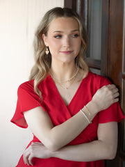 Woman in a red dress with jewelry standing indoors.
