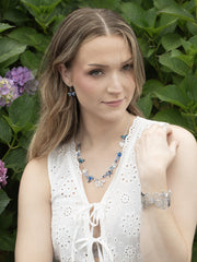Woman wearing a white sleeveless top and jewelry against a green leafy background