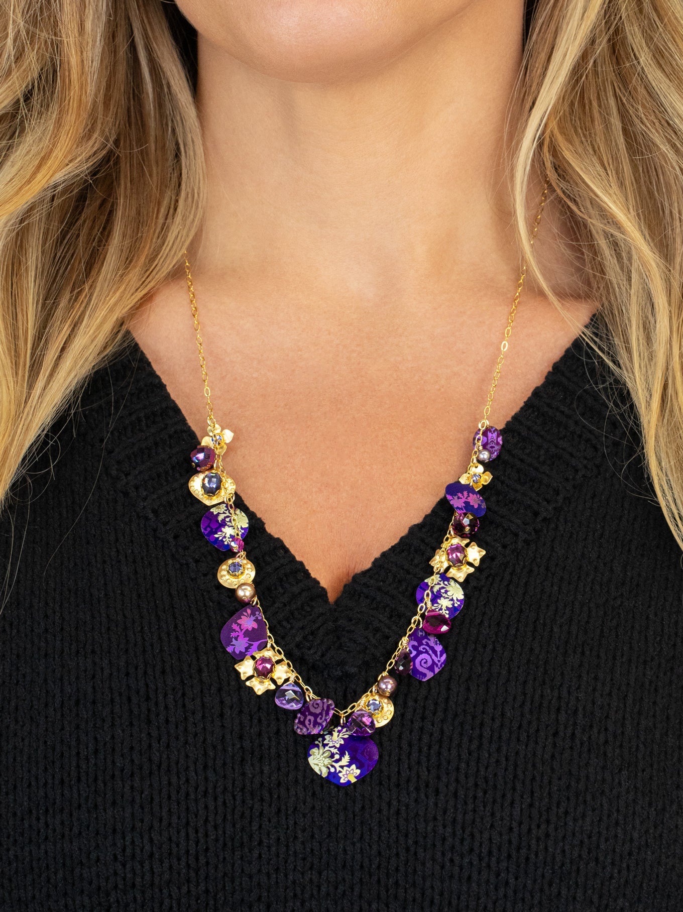 Necklace with purple and gold beads worn by a person against a black background