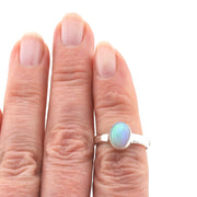 Silver ring with an opal stone on a hand against a white background