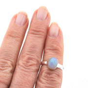Silver ring with a light blue gemstone on a finger against a white background