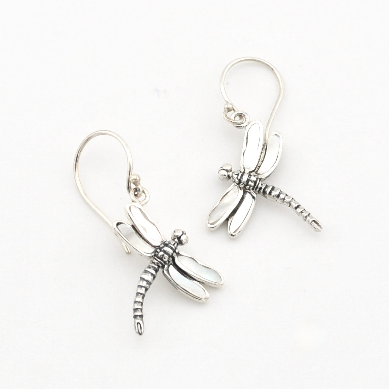 A pair of silver dragonfly drop earrings with textured wings and hooks, displayed on a clean white background.