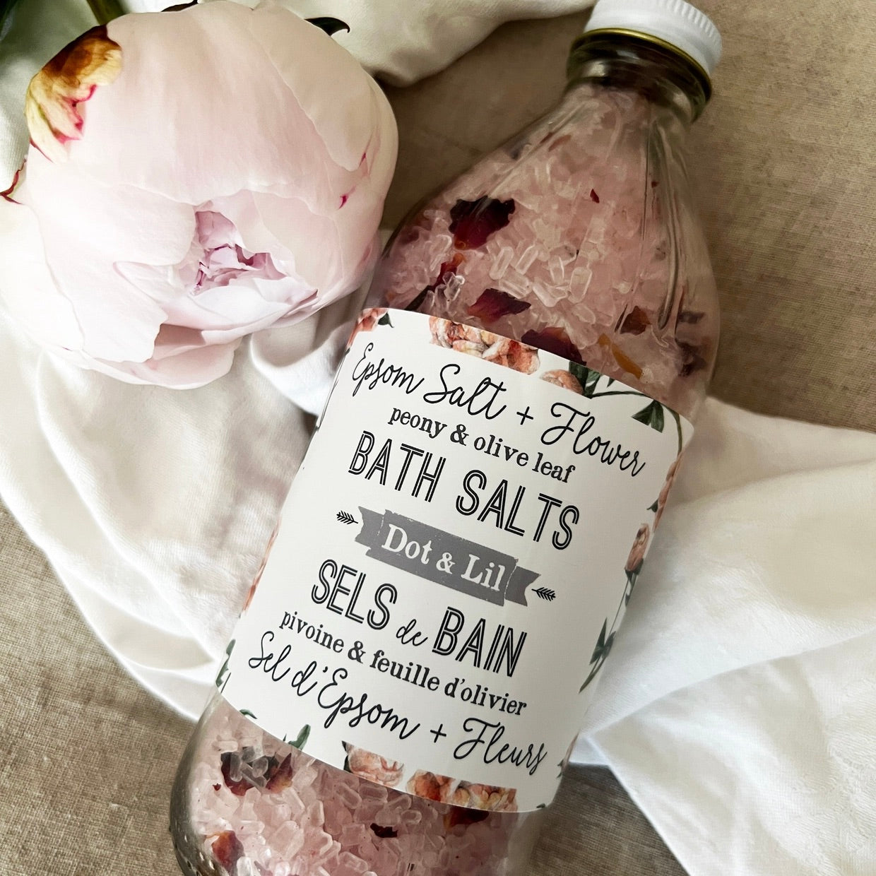 Bottle of bath salts with a label and a pink flower on a textured surface