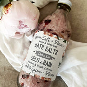 Bottle of bath salts with a label and a pink flower on a textured surface