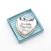 Heart-shaped silver trinket with 'You make my heart smile' text in a striped box