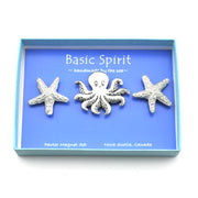 A three-piece pewter magnet set by Basic Spirit, featuring a central octopus and two starfish, displayed inside a light blue gift box with a blue insert card.