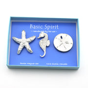 A three-piece pewter magnet set featuring a starfish, a seahorse, and a sand dollar, presented in a light blue box with a blue insert. The insert features the brand name 'Basic Spirit' and 'handmade by the sea~'.