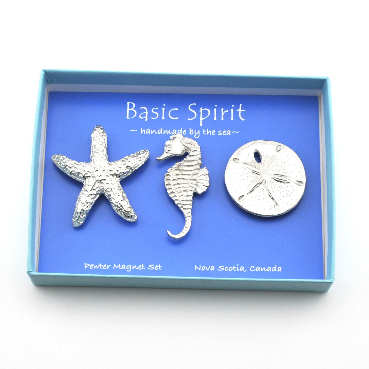 A three-piece pewter magnet set featuring a starfish, a seahorse, and a sand dollar, presented in a light blue box with a blue insert. The insert features the brand name 'Basic Spirit' and 'handmade by the sea~'.