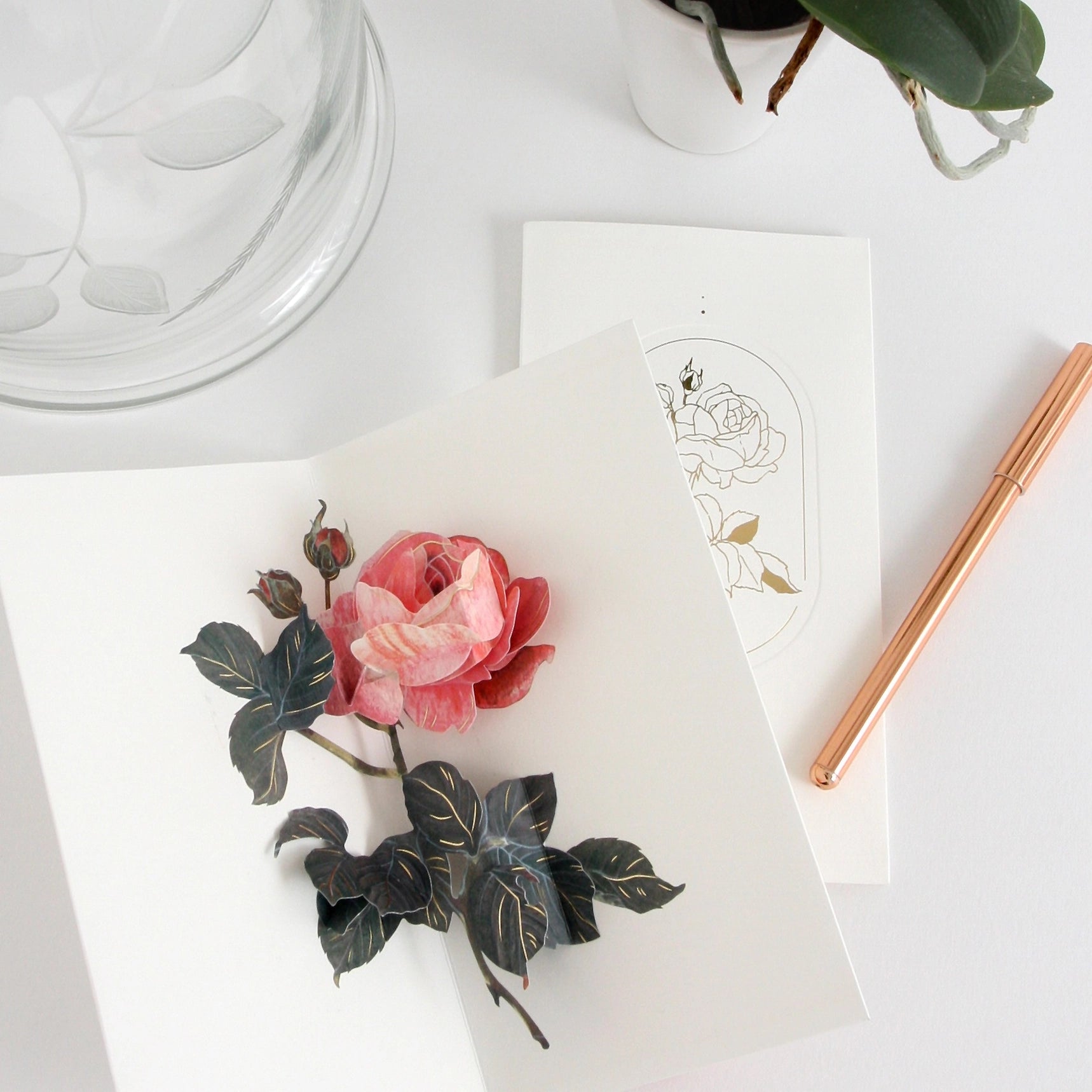 Decorative paper flower on a white surface with a pen and plant in the background
