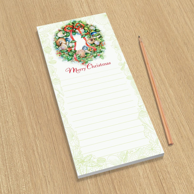 Notepad with Christmas wreath design and 'Merry Christmas' text on a wooden surface.