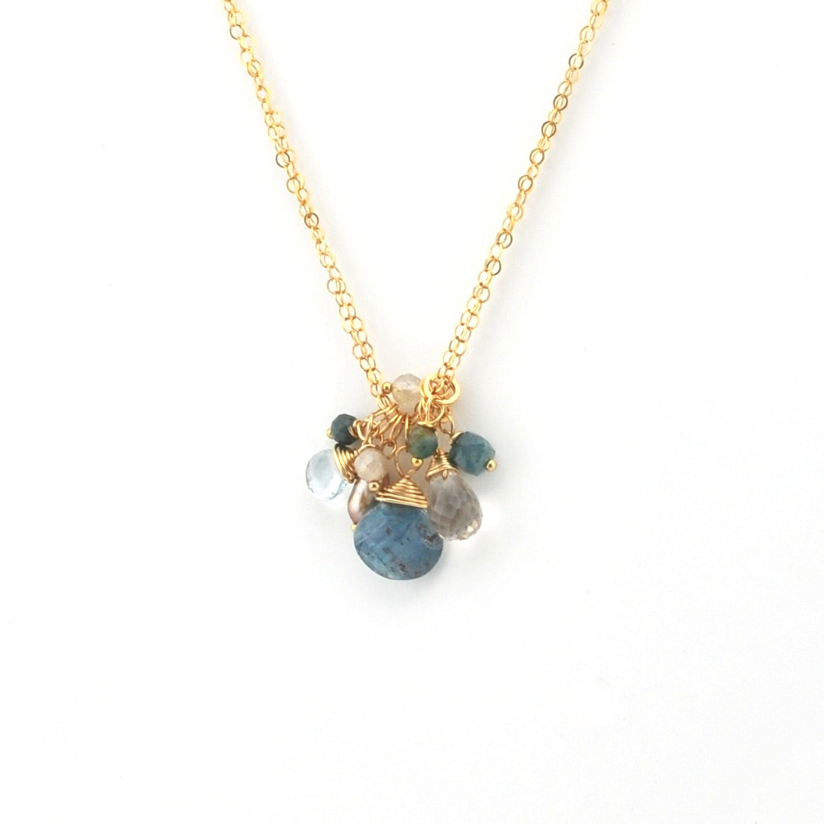 A delicate gold chain necklace featuring a cluster pendant with a large blue stone, smaller green and gray stones, and gold wire accents, set against a plain white background.